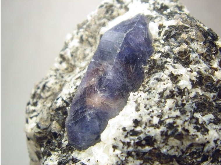 Um cristal de coríndon de 26x7 mm mostrando uma cor azul profundo depositado no fundo de um ninho de feldspato potássico branco. Foto e coleção de Antonio Borelli. Mindat.org.